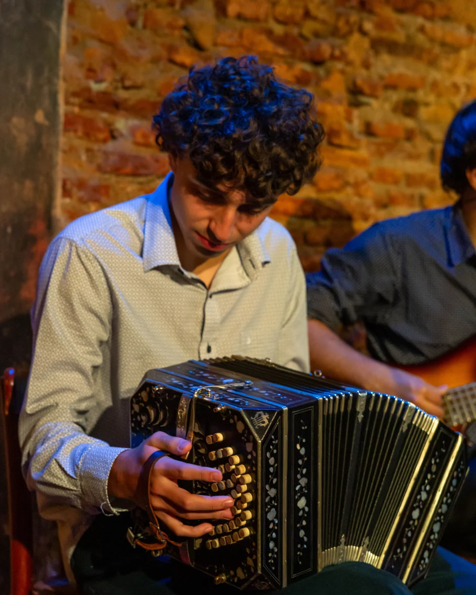 A bandoneon player's hands working the instrument's keys in a warmly lit room